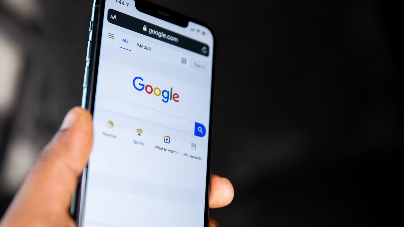 A hand holding a smartphone showing the Google search homepage