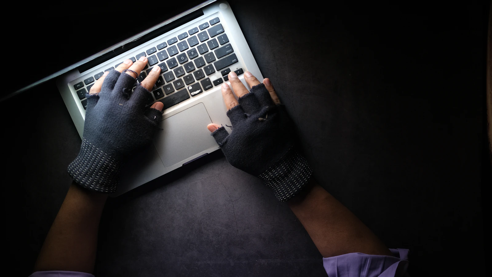 A person in fingerless gloves typing on a laptop in the dark, representing a hacked WordPress site