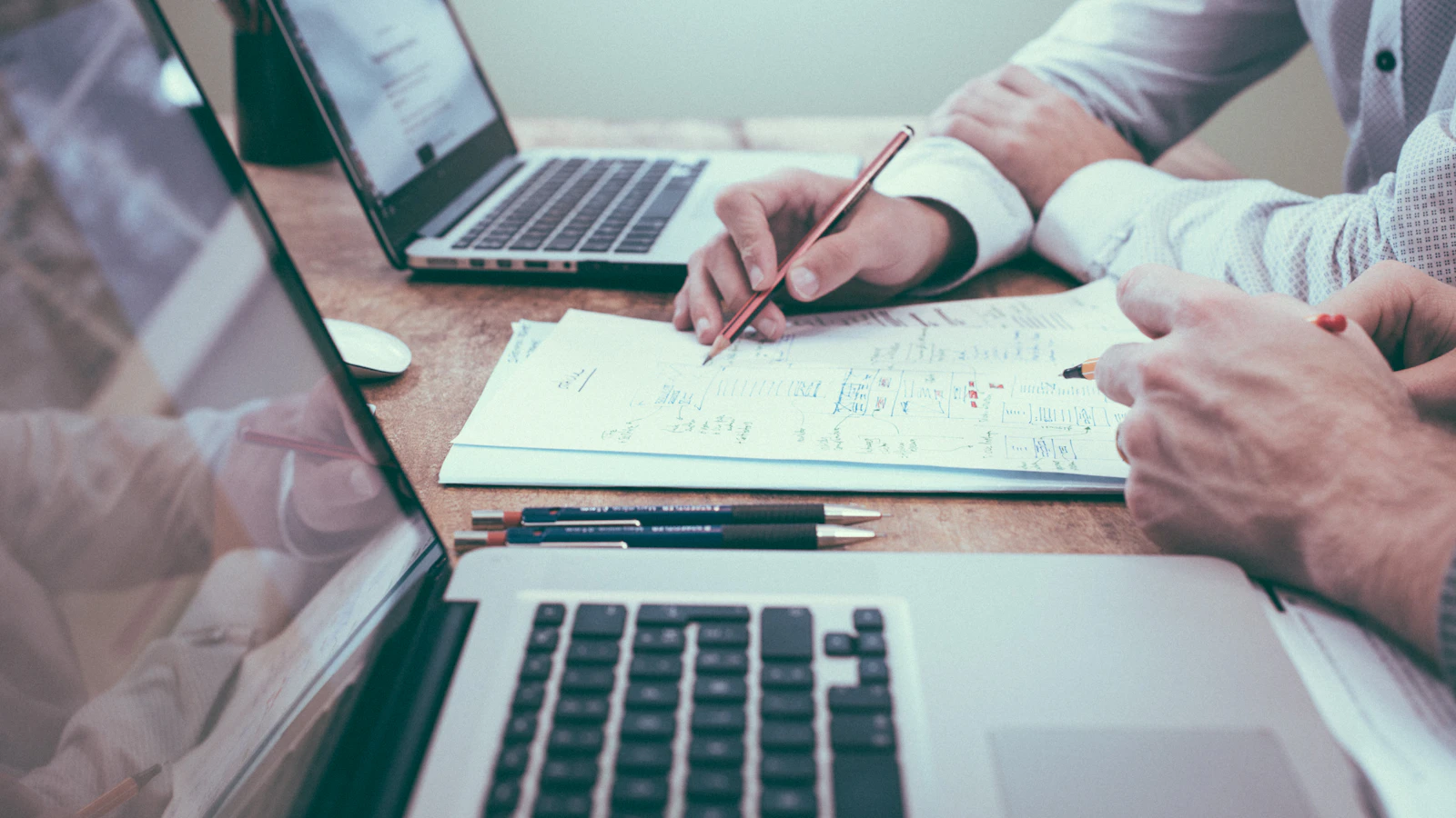 A person making notes with a pencil next to a laptop, planning a website project