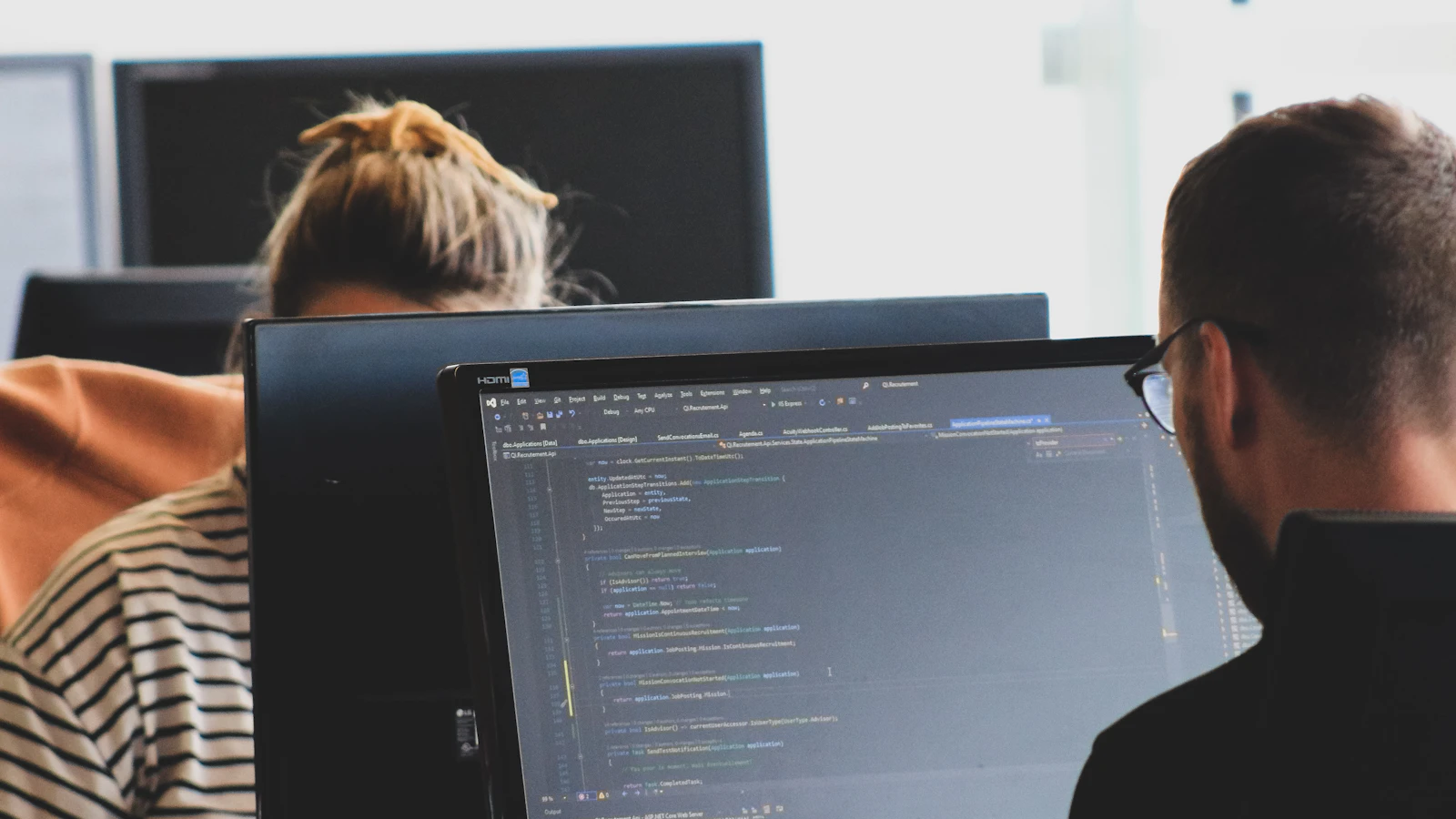 Two people working on code at computer monitors in a bright office