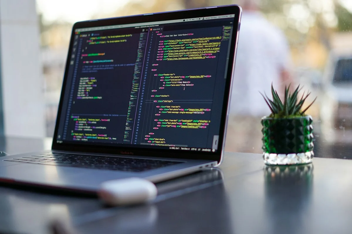 Laptop showing code on a desk beside a plant
