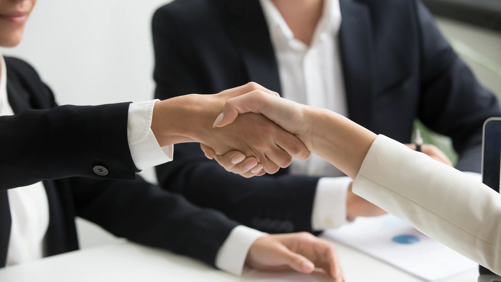 Two people shaking hands in front of a laptop, representing a website handover
